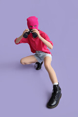 Young woman in balaclava with binoculars on lilac background