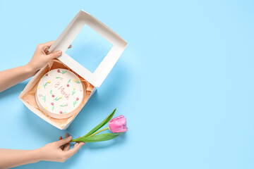Female hands with sweet bento cake and beautiful tulip on blue background. International Women's Day