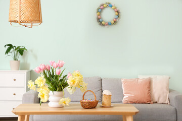 Beautiful tulips with Easter basket and cake on table in living room