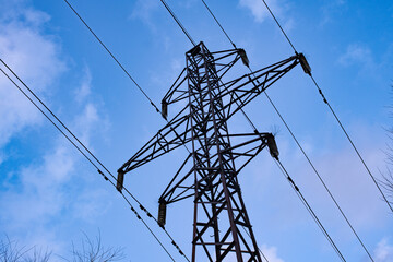 Metal support of an overhead electrical transmission line with lightning protection against a background of blue sky, clouds and tree branches. Side view from the ground. - obrazy, fototapety, plakaty