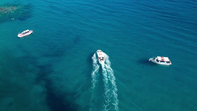 Aerial view of sailing boat with white foamy trail in blue transparent water
