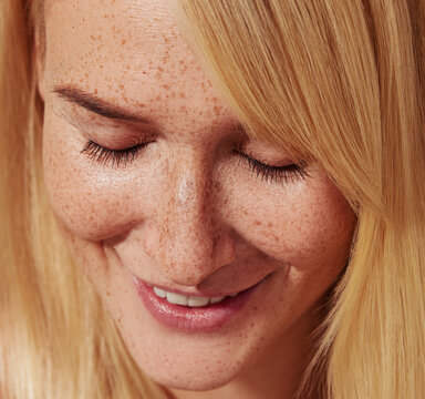 Close-up of smiling blond female with freckles looking down. Highly detailed close-up shot of a young female with smooth freckled skin.