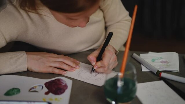 Close-up. A woman draws a Father's Day greeting card with a marker while sitting at the table in the living room. DIY Father's Day greeting card