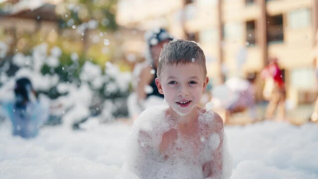 Little man having fun on a foam party. Children boy dancing and playing in the white foam, bathe in a soapy disco outdoors. Festival, birthday celebration for children, entertainment concept.