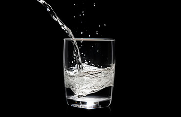 Water pouring into glass on the black background
