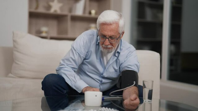 Senior man measuring pressure at home. Old male measuring blood pressure with electronic tonometer, have health problem making. Hypertension hypotension problem, self-care, pensioner health concept.