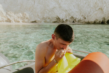 A young guy inflates a lifebuoy while sitting in a boat.