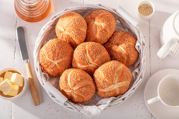 Homemade Kaiser rolls with sesame seeds in white basket.