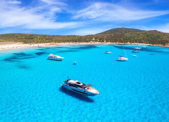 Aerial view of luxury yachts on blue sea at sunny day in summer. Sardinia, Italy. Aerial view of speed boats, yachts, sea lagoon, shore, transparent water, sky. Top view from drone. Tropical seascape	