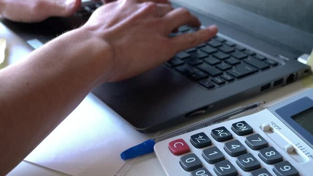 電卓で計算し、パソコンに入力している若い男性会計士の手元のクローズアップ