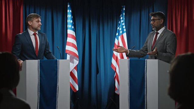 Medium full footage of Indian and Caucasian male politicians standing at rostrums on stage in hall, arguing while participating in American Senate election debate, interrupting, gesticulating, blaming
