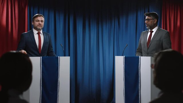 Medium shot of two American politicians participating in election debates - Caucasian male majority leader outlining economic policy, and Indian opposition candidate criticizing and challenging him