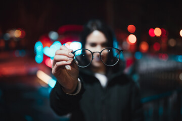 A girl who can't see well holds her glasses in front of her. Blurred background and bokeh lights....