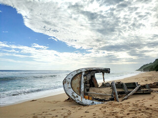 The wreckage of a wooden ship on a sandy beach on the ocean. The shipwreck