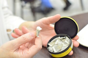 A box of snus pads replaces smokeless cigarettes. Swedish nicotine pouch. A woman holds one bag of...