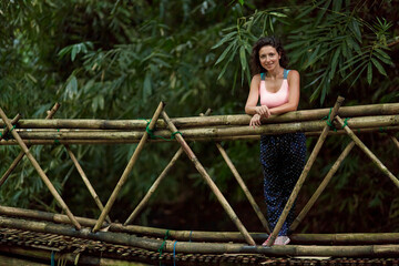 A young woman stands on a suspended bamboo bridge in the jungle on the popular island of Bali.