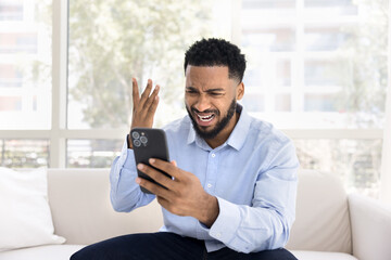 Concerned desperate young Black man having problems with cellphone, disappointed with online...