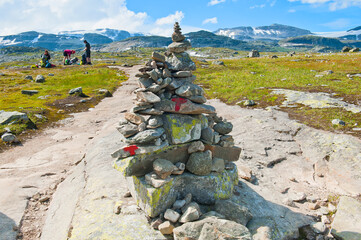 Beautiful landscape with mountains, tourists and the path marked by stone cairn and red T letters on the trail to The Blue Ice (Blaisen) ice field located in Hardangerjokulen glacier in Finse, Norway - 749627716