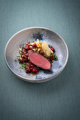 Traditionally roasted saddle of venison fillet with spätzle, vegetable and fruits in chocolate red wine sauce served as close-up on a Nordic design plate with copy space 