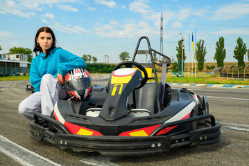 young girl racer with a helmet sits near a racing kart