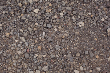 Background image of the surface covered with small gravel on the ground. Wallpaper. Substrate for text. Detailed texture of fine pebbles on the ground. The surface of the hiking trail. Top view.