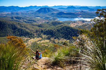 Obraz premium backpacker enjoys the panorama of mount barney national park and lake maroon from the summit of mount may; hiking mountain in south east queensland, australia