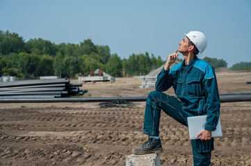 Caucasian male builder in hardhat holding laptop at construction site. 