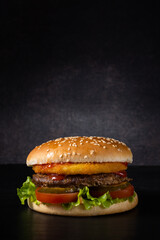 fresh burger with sesame bun and beef patty on a dark background with a gradient spot of light. vertical photo with copy space. side view