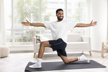 Happy athletic young African man exercising at home, training body on yoga mat, enjoying fitness...