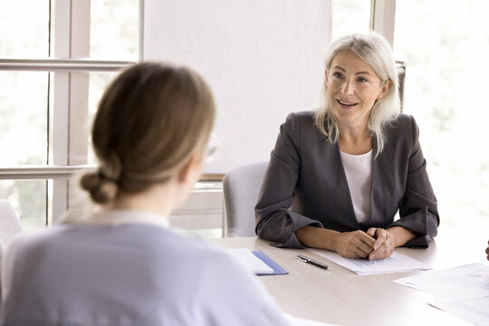 Mature businesswoman negotiates to client during meeting in office, lead training or seminar listen teammate ideas, search solution. Job interview in conference room, HR manager interviewing applicant