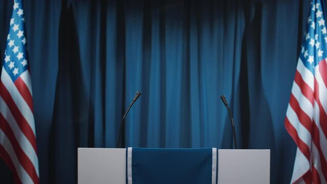 Medium panning no people footage of podium or rostrum on stage in hall or TV studio with American flags, set up for public debates during presidential election campaign