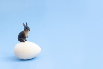 Toy rabbit sitting on a huge egg. Minimal creative Easter concept. Selective focus, copy space