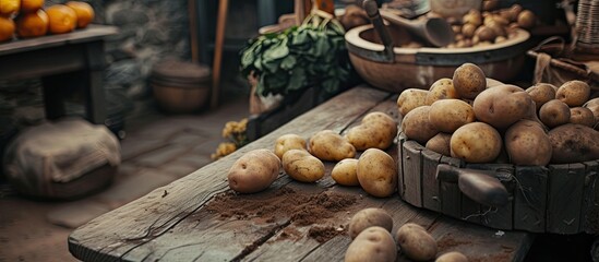 A wooden table is covered with a variety of potatoes, ranging in size and color. The potatoes are arranged in a messy pile, some with dirt still clinging to them, creating a rustic and earthy scene. - obrazy, fototapety, plakaty