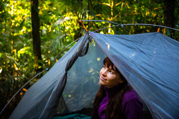 pretty girl sitting in a transparent tent and admiring unique rainforest at remote bush campground...