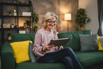 Obraz premium mature blonde woman with eyeglasses use digital tablet at home