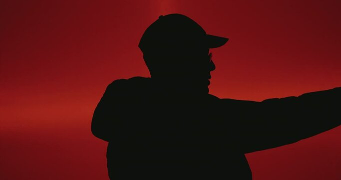 Silhouette of Red Background With Man wearing Cap. A man in a cap silhouetted against a red background offers a minimalist yet striking image, where the vivid backdrop accentuates the silhouette's out