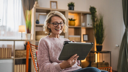 mature blonde woman with eyeglasses use digital tablet at home