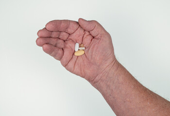 Caucasian male hand holding four medicine capsules on white background