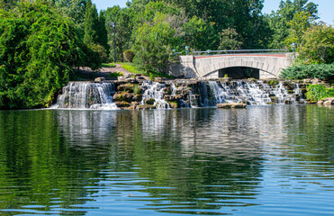 Fototapeta na wymiar Waterfalls reflected in pond with stone bridge and trees
