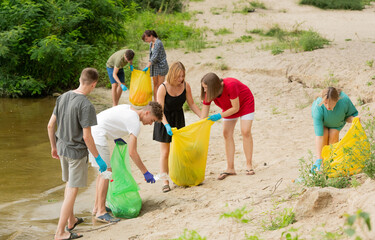 a group of young people, student volunteers, cleaning up trash on the beach - 749656776