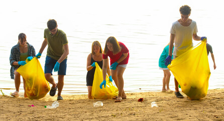 a group of young people, student volunteers, cleaning up trash on the beach - 749656779