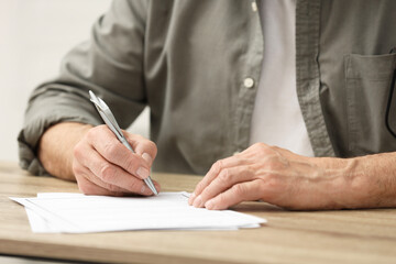 Senior man signing Last Will and Testament at wooden table indoors, closeup