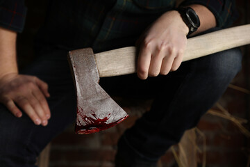 Man holding bloody axe indoors, closeup view