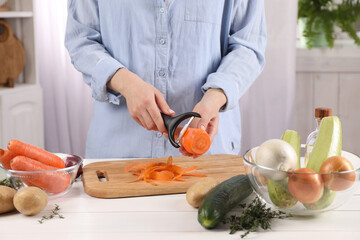 Woman peeling fresh carrot at white wooden table indoors, closeup