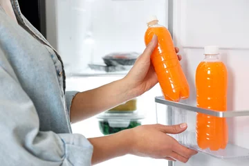 Deurstickers Young woman taking bottle of juice out of refrigerator, closeup © New Africa