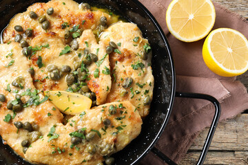 Delicious chicken piccata with herbs and lemon on wooden table, top view