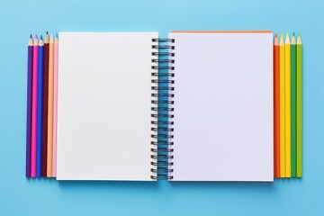 An open white notebook surrounded by pencils on a multicolored surface. Open Notebooks with Rainbow-Colored Pencils