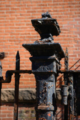 Rustic metal fence pole in front of the red brick wall, close-up