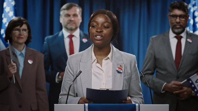 Medium shot of young African American female politician campaigning for presidential or governor nomination from US Republican Party addressing voters at tribune, ending speech, thanking and waving