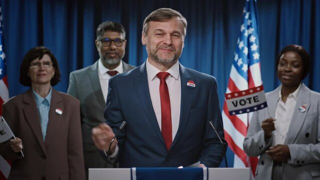 Medium footage of mature Caucasian male US president or senator candidate wrapping up his keynote election speech at Democratic Party convention, waving to public, smiling and leaving